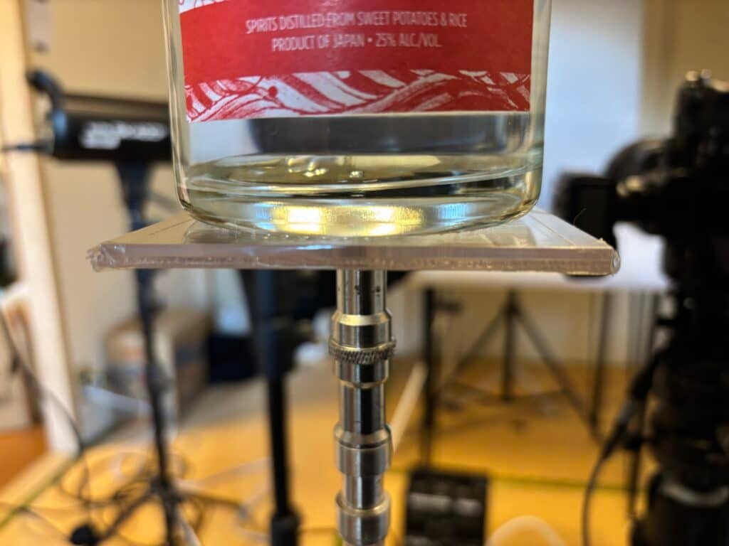 A bottle support plate on a light stand, supporting a full glass bottle.