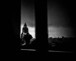 Silhouette of a large seated Buddha in Bangkok, Thailand, set against the darkness of an afternoon thunderstorm